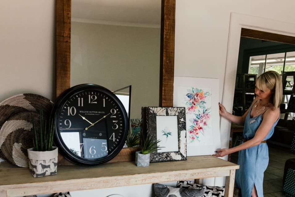 Woman arranging a floral watercolour beside a large clock on a shelf