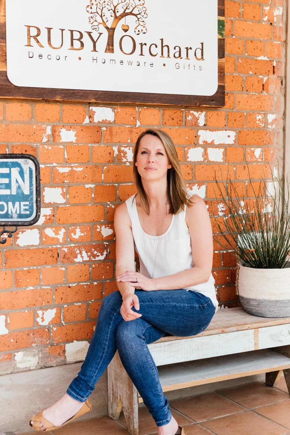 Woman sitting on a bench under The Ruby Orchard sign