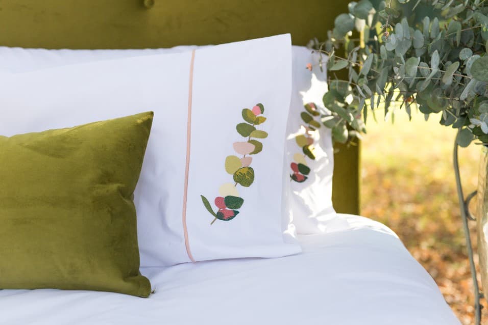 Embroidered pillowcase and green velvet cushion on a bed
