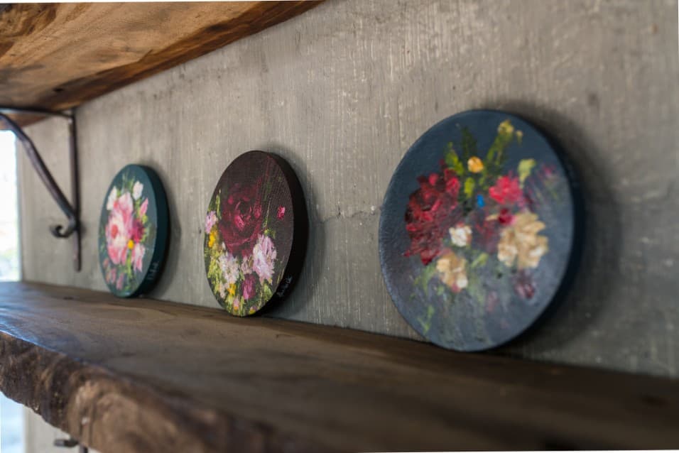 Three round floral paintings on a rustic shelf