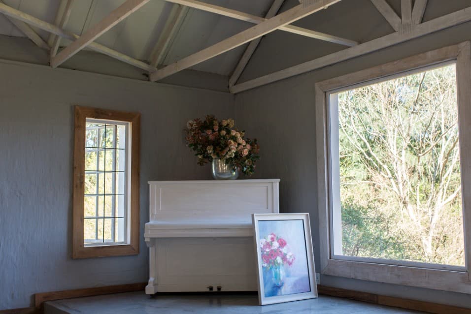 Rose painting beside a white piano in a sunlit room