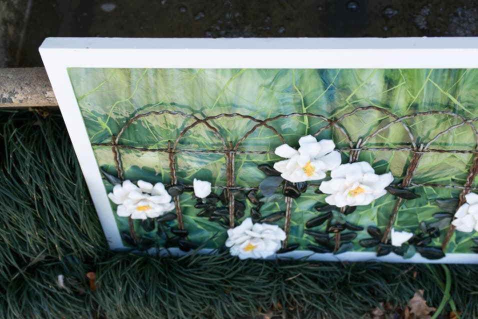 Painting of white roses on a fence, displayed outdoors