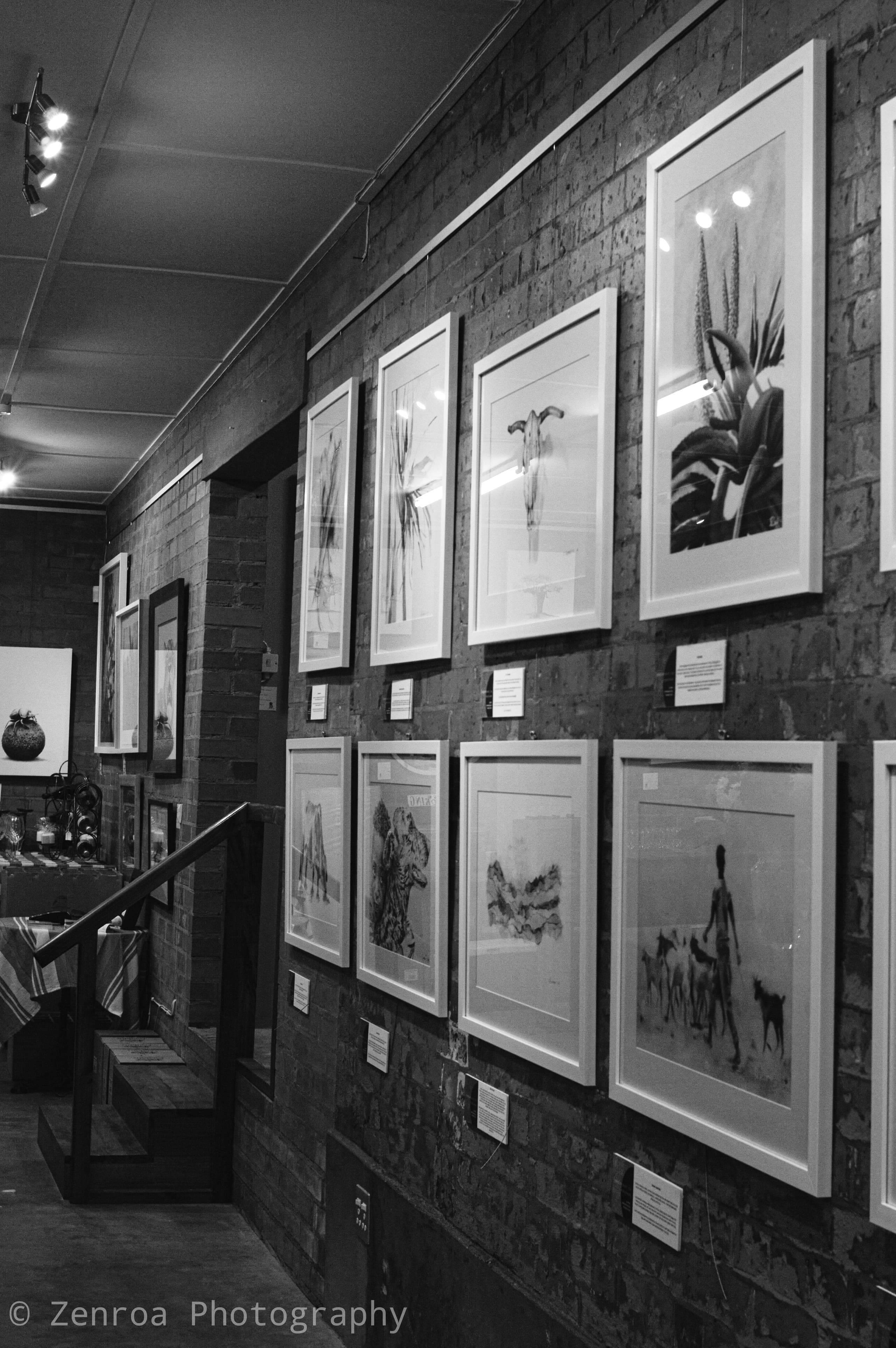 Framed monochrome artworks along a brick gallery wall