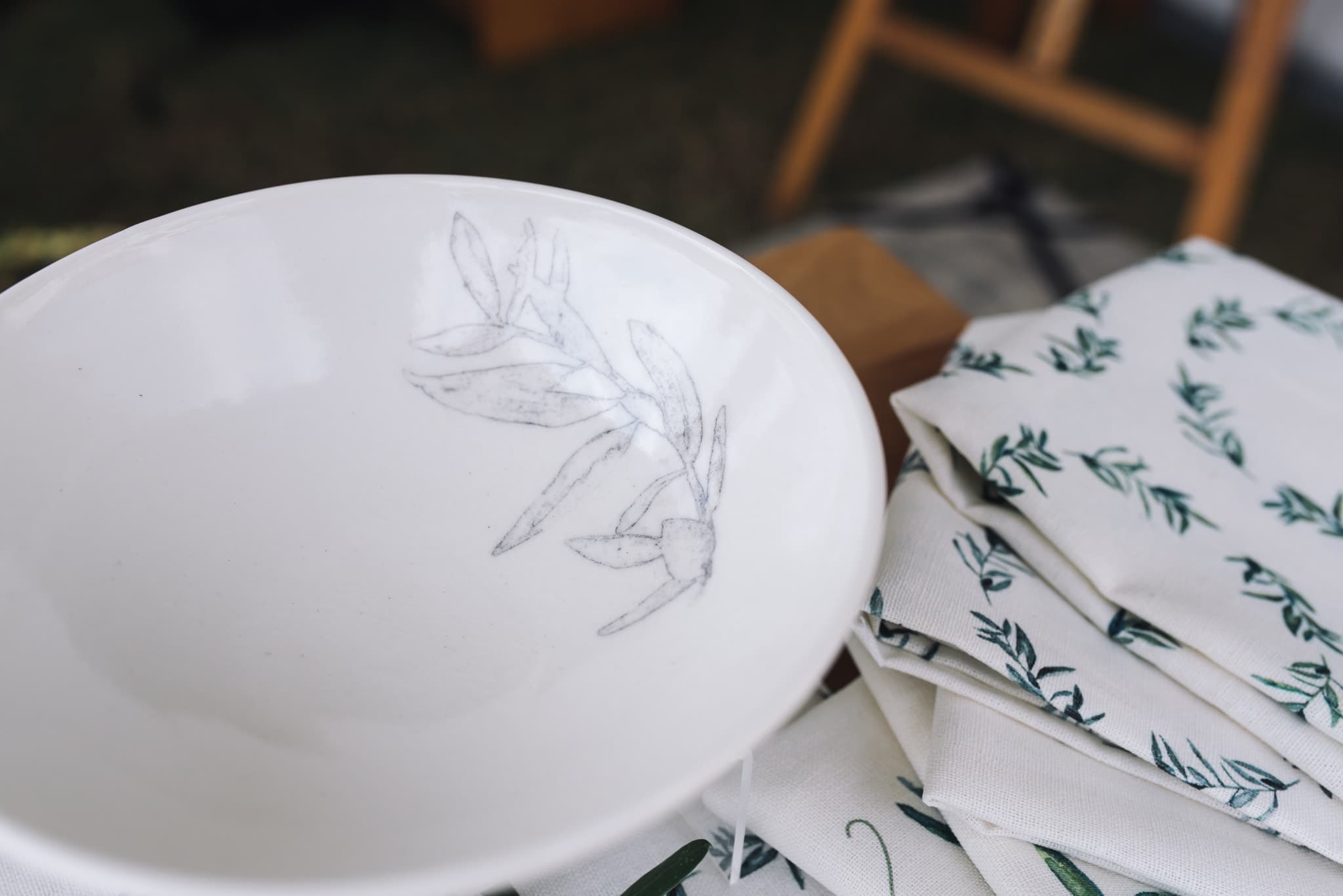 Olive-branch ceramic bowl beside folded olive-print napkins