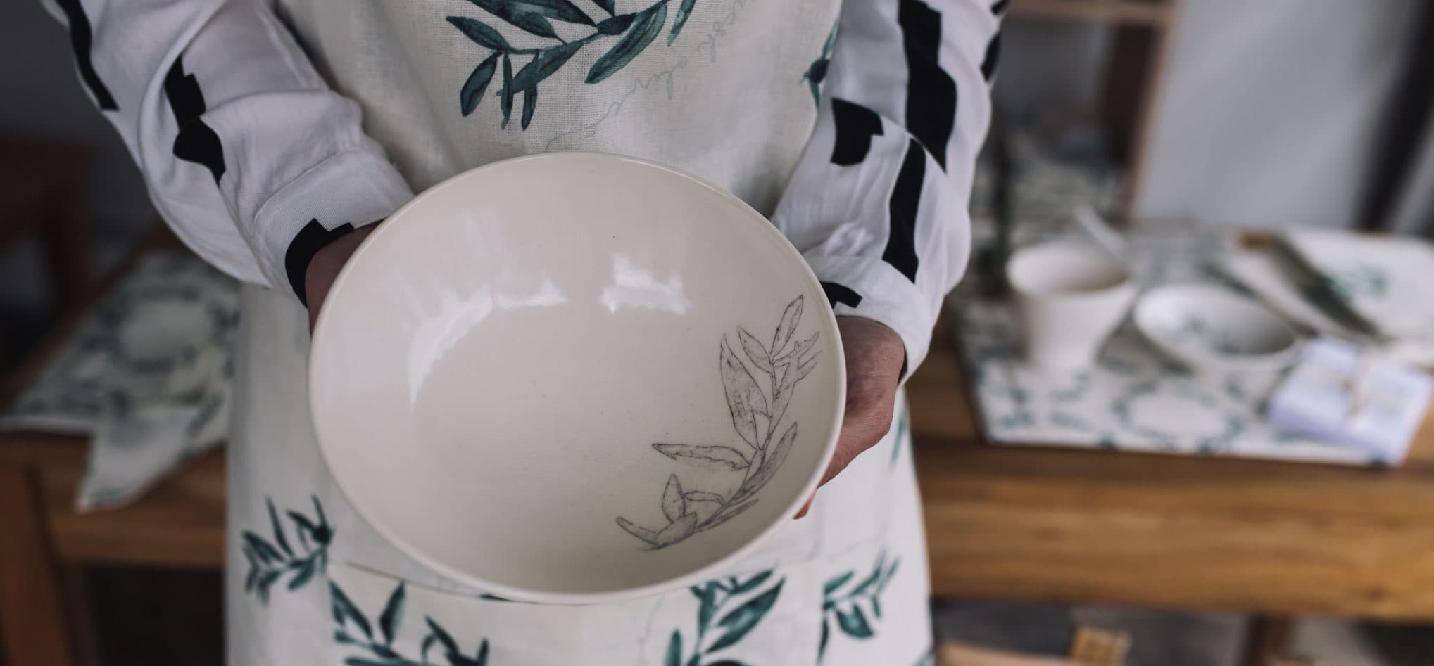 Olive-branch ceramic bowl held over olive-print linen